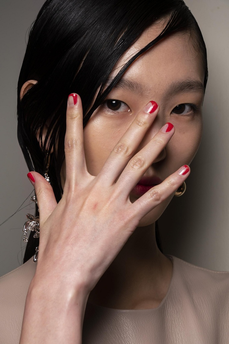 ragazza con unghie corte dipinte a meta manicure di colore rosso capelli raccolti