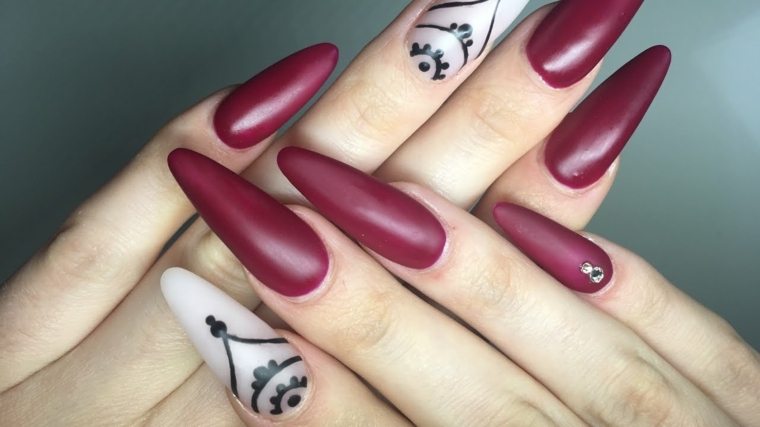 nails rosse scure con finitura opaca, indice bianco latte con decorazioni nere