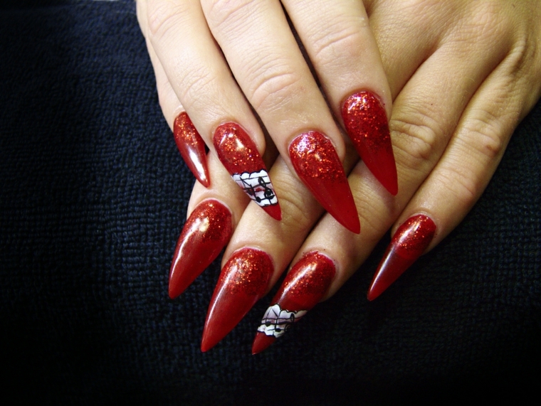 manicure con smalto rosso glitterato e alcune decorazioni bianche e nere sull'anulare